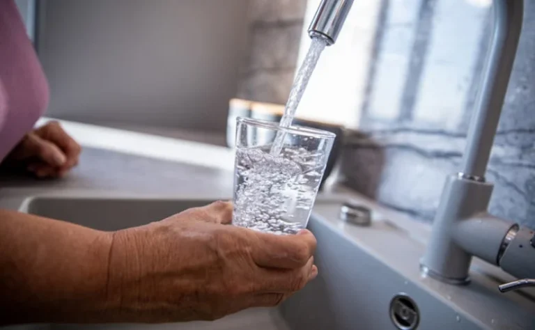 a woman pouring water from a sink into a glass cup