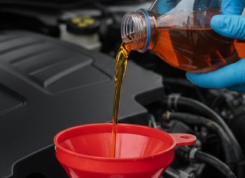 worker pouring brake fluid into a car through a funnel